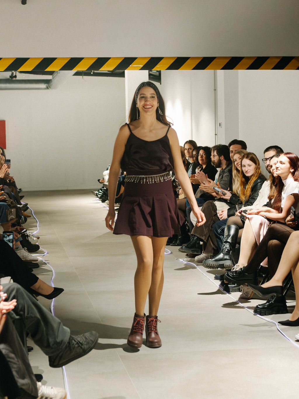 Model walking on a fashion show runway wearing Luna top and Serena Skirt, with an audience seated on either side.