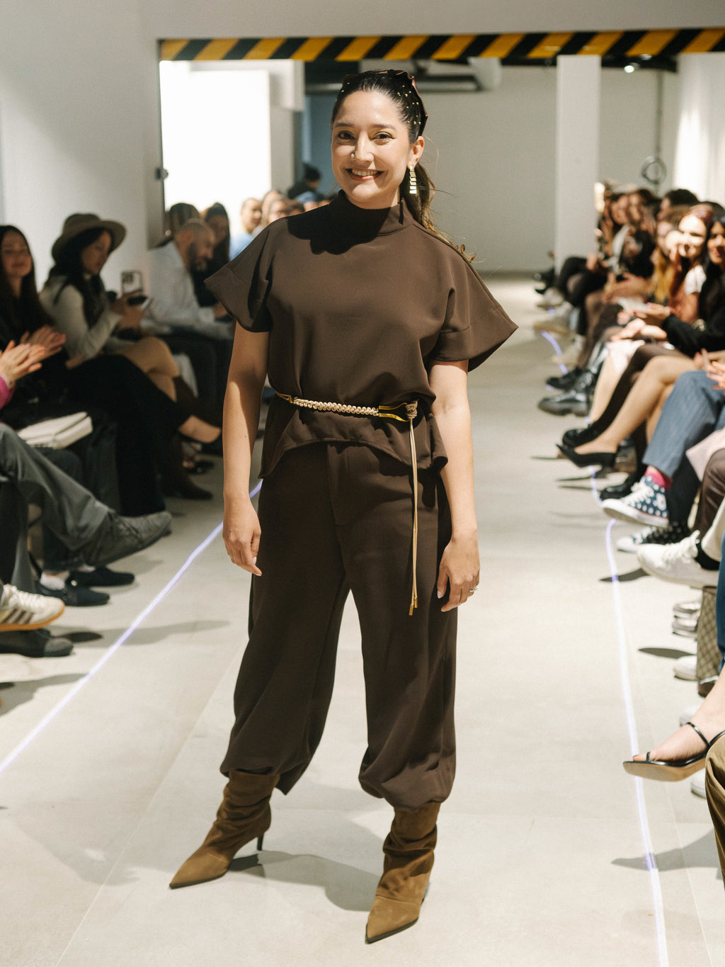 Model wearing The Diva and Bossy outfit on a fashion show runway with an audience.