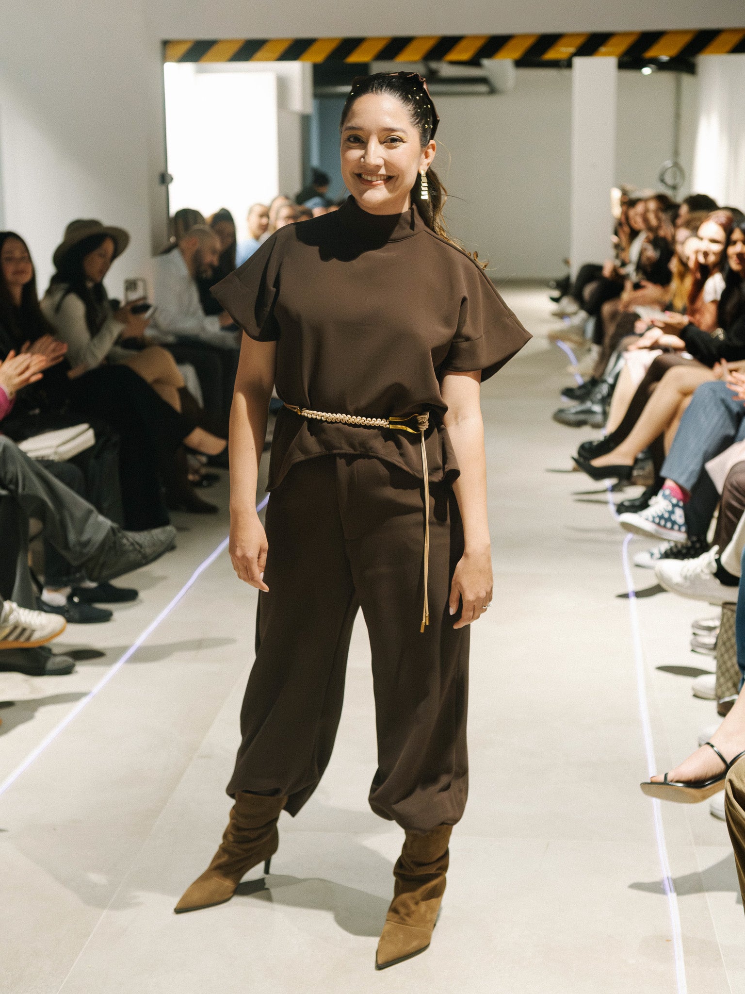 Model wearing The Diva and Bossy outfit on a fashion show runway with an audience.